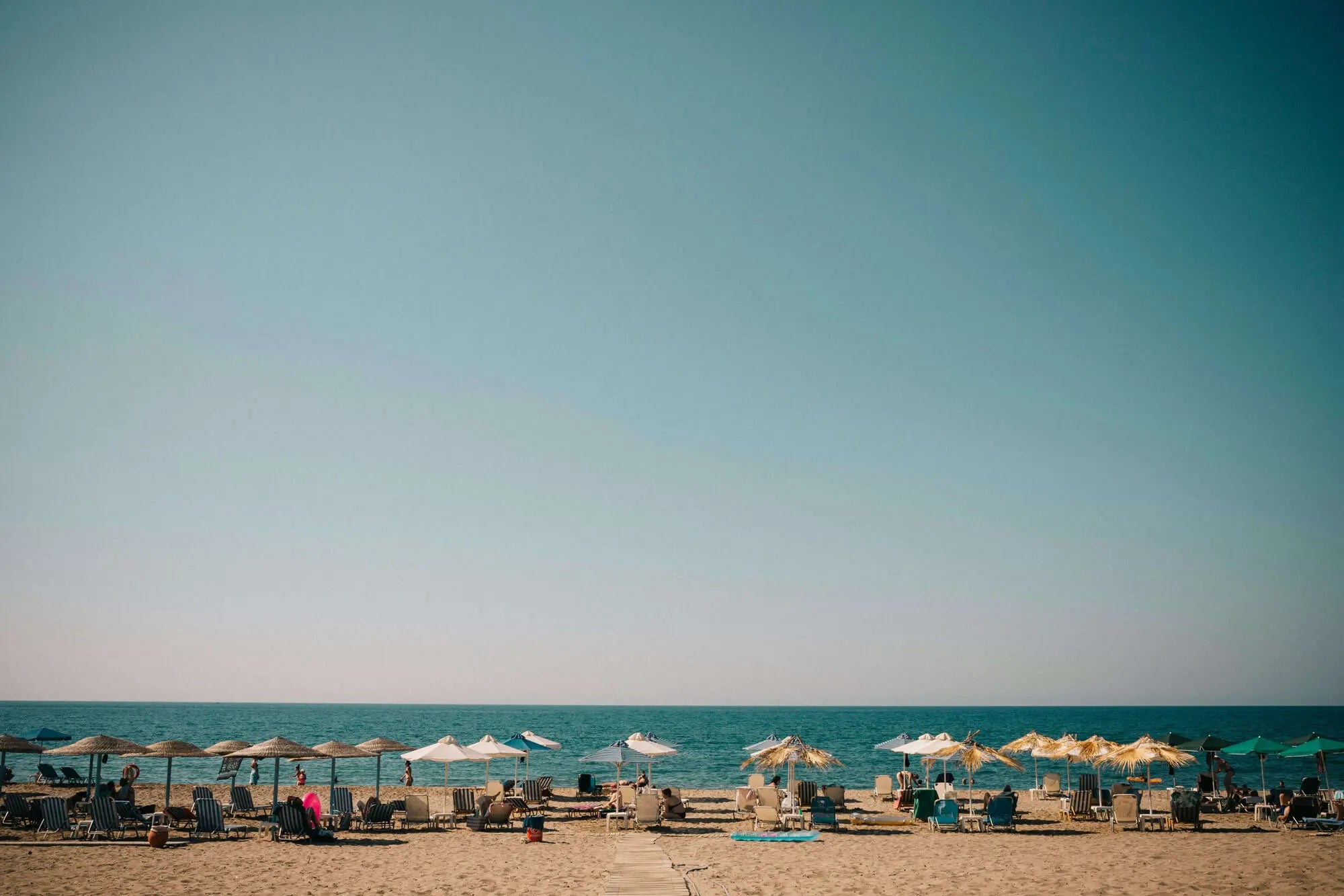 Beach scene with umbrellas and chairs under a clear blue sky.